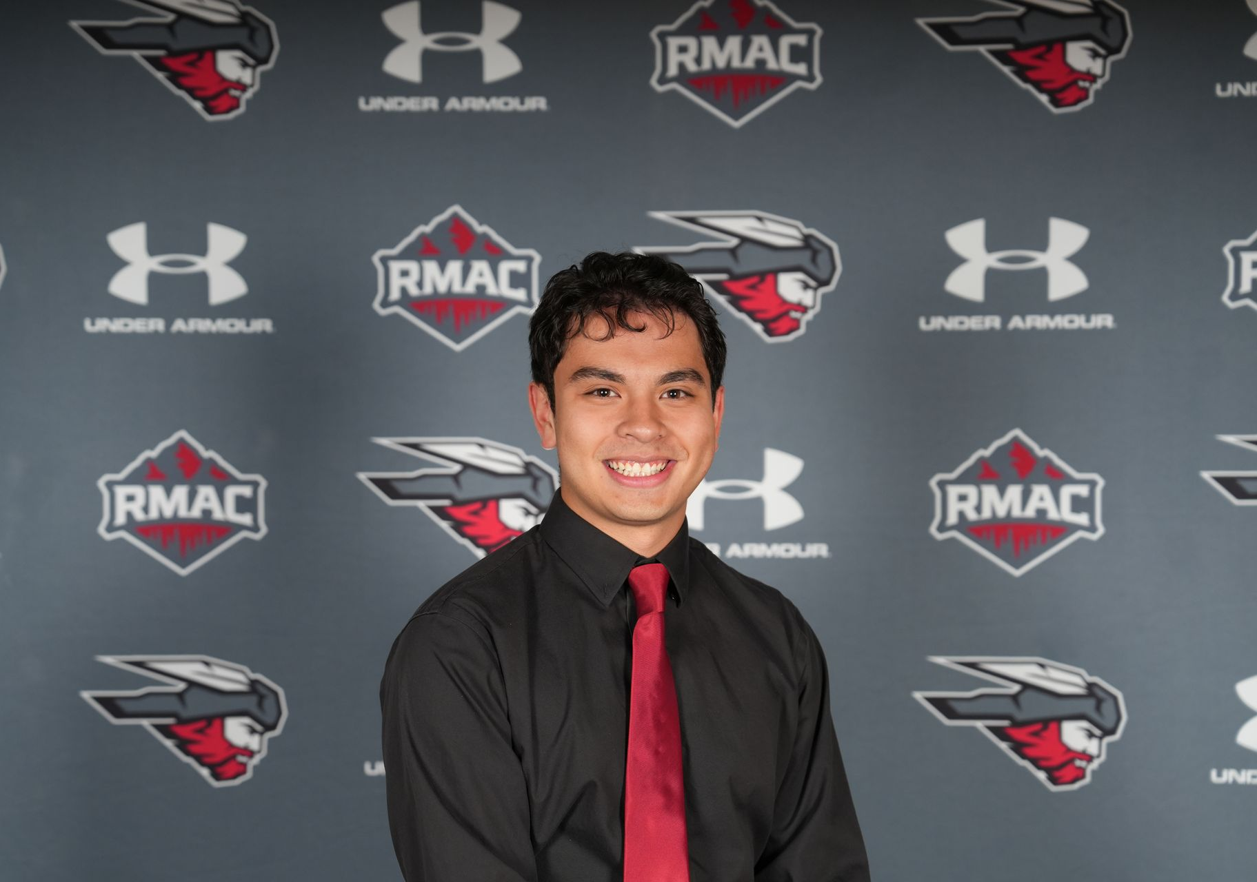 Kai Vong in a black shirt and red tie posing in front of a gray background with logos.