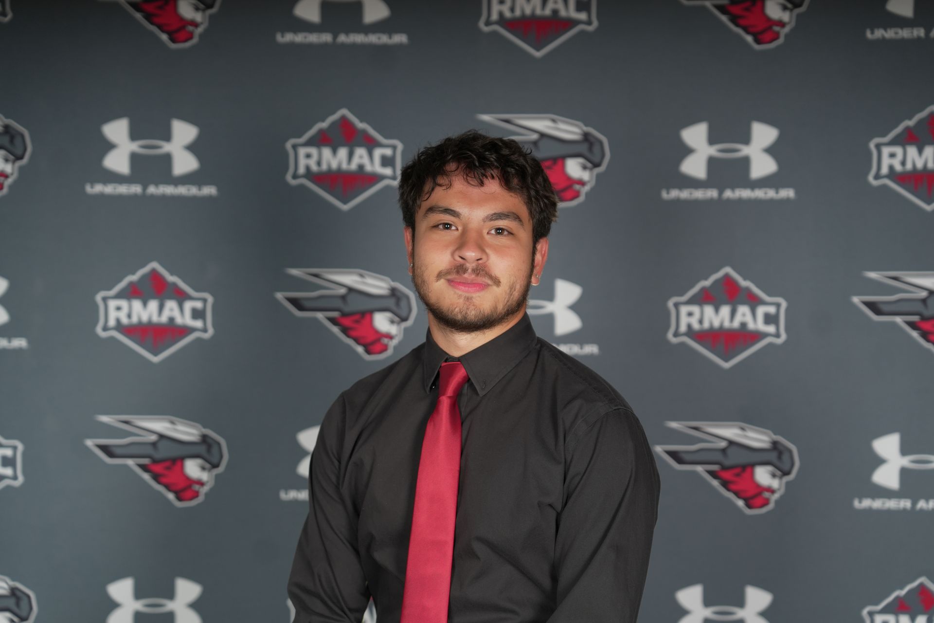 Kai Vong in a black shirt and red tie posing in front of a gray background with logos.