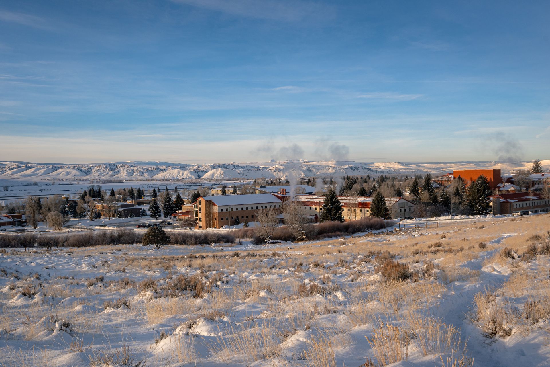 Snow-covered landscape with buildings in the distance under a clear blue sky.