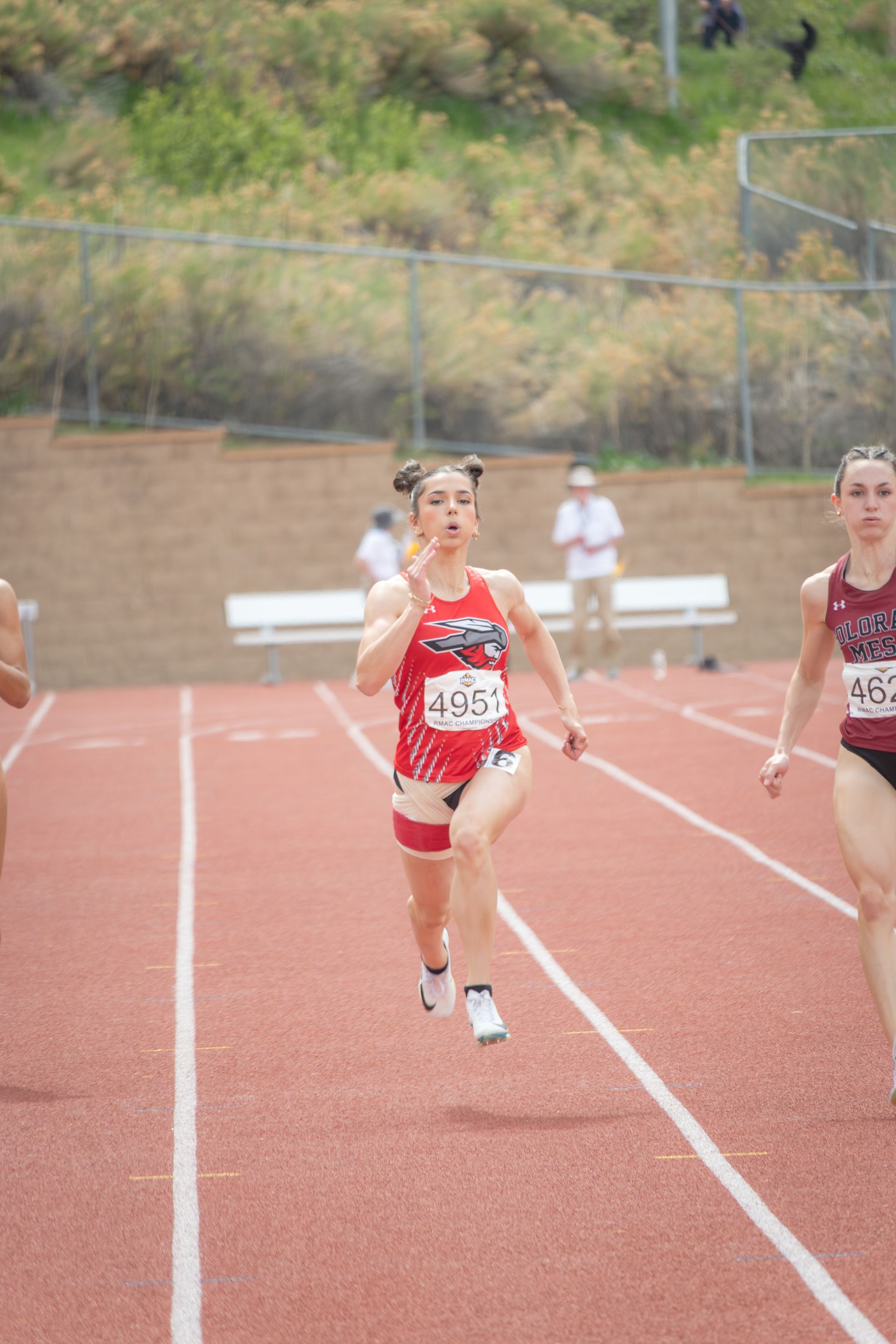 Female track athlete in a red and white uniform running on a red track, focused expression.