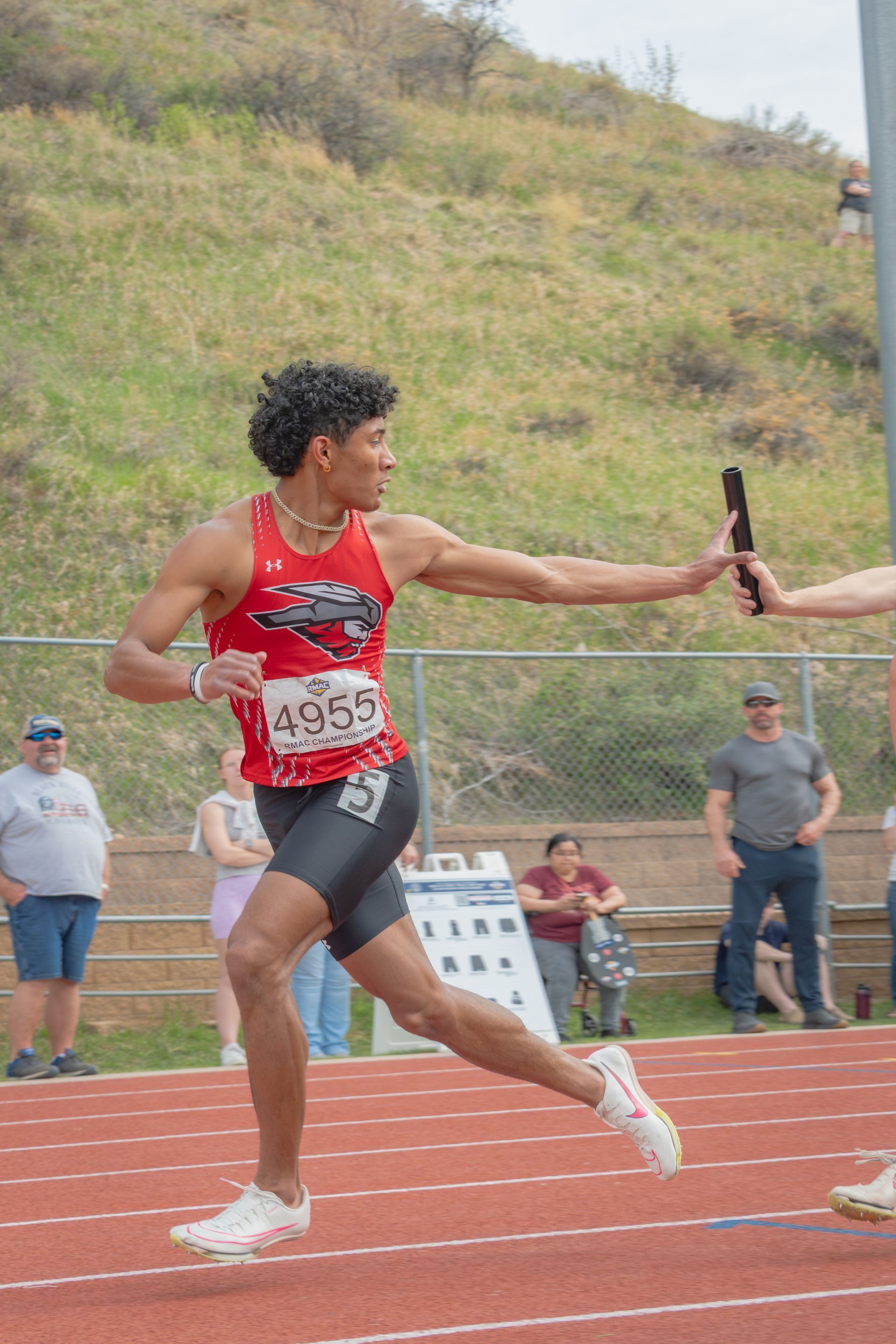 Track athlete in red singlet and black shorts receives baton on a track.
