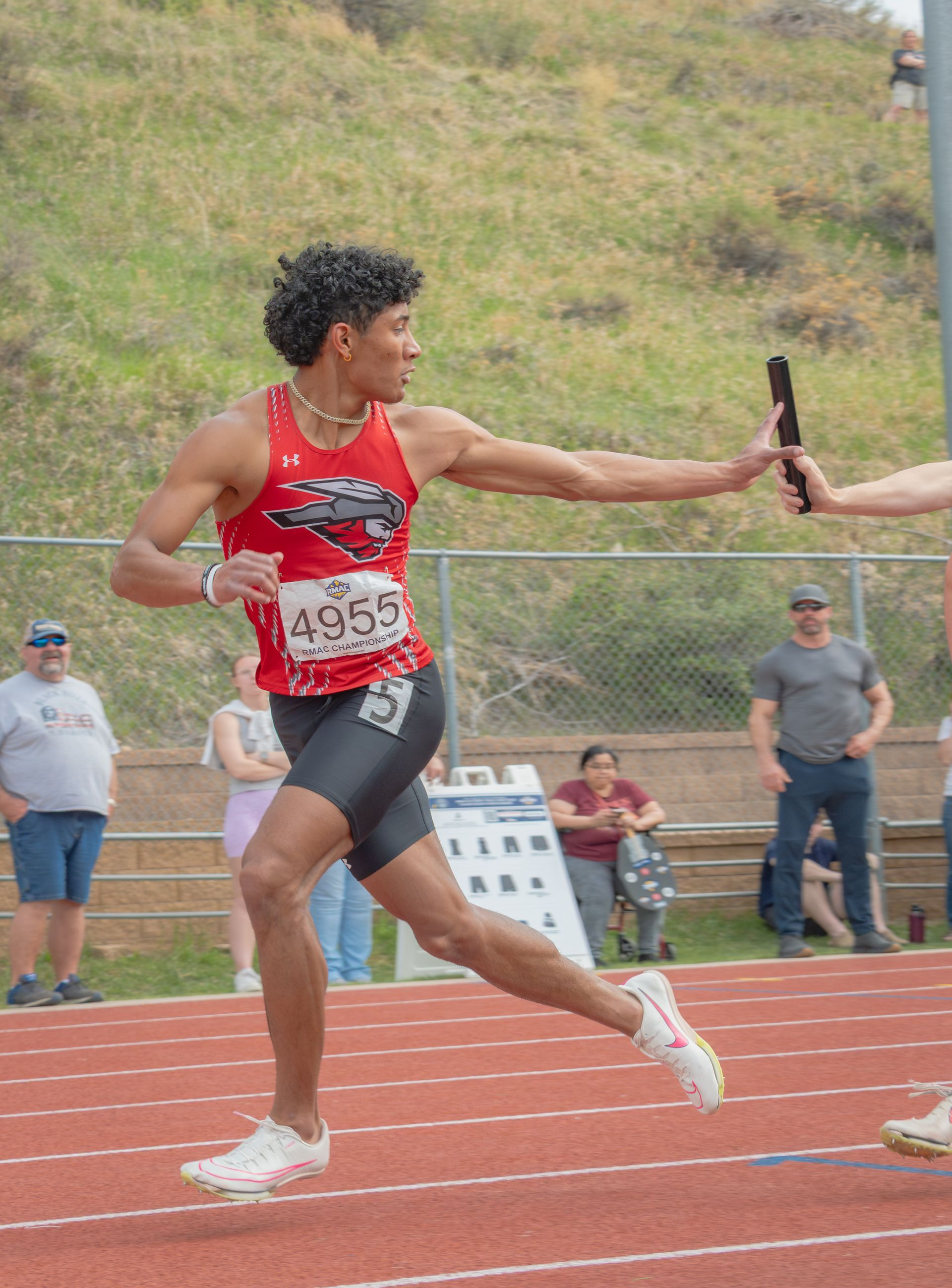 A young man in red and black uniform, running a relay race, receiving the baton on a track.