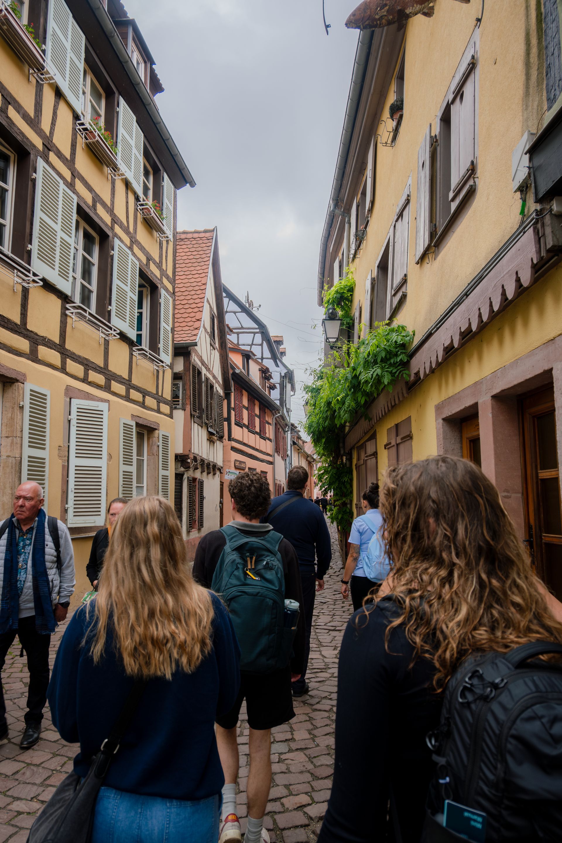 People walking down a narrow cobblestone street lined with colorful, old buildings in Europe.