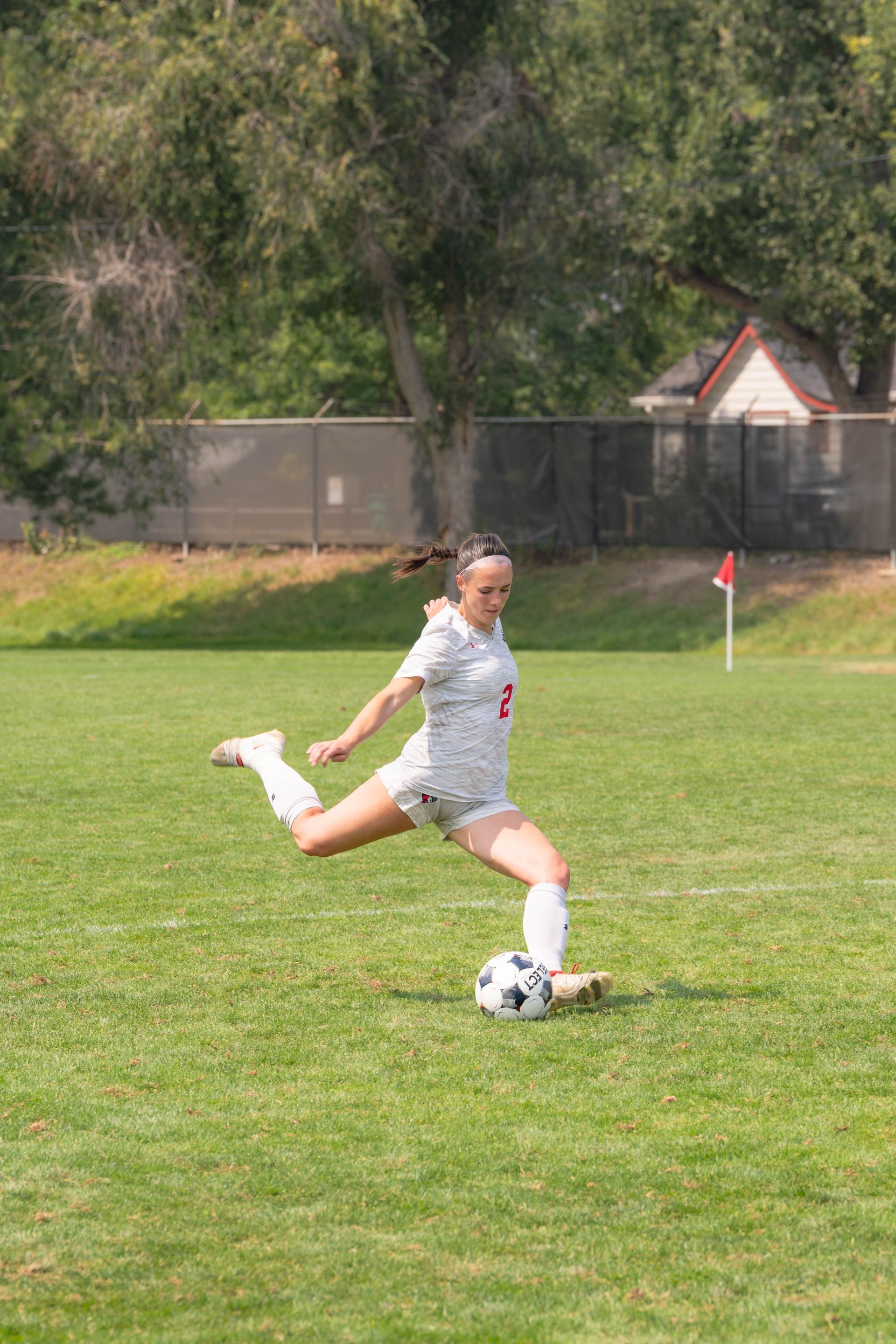 Soccer player in a white uniform kicks a black and white soccer ball on a green field.