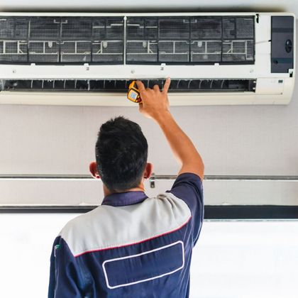 A man is working on an air conditioner with a tape measure.