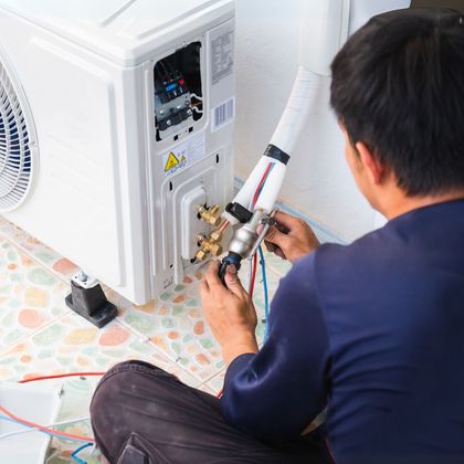 A man is sitting on the floor working on an air conditioner.