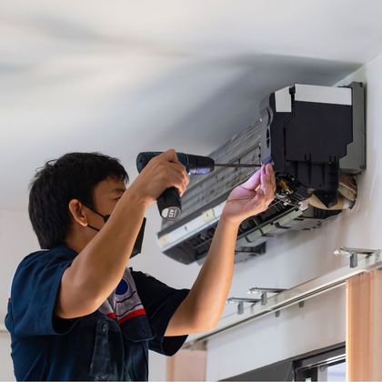 A man wearing a mask is fixing an air conditioner with a screwdriver.