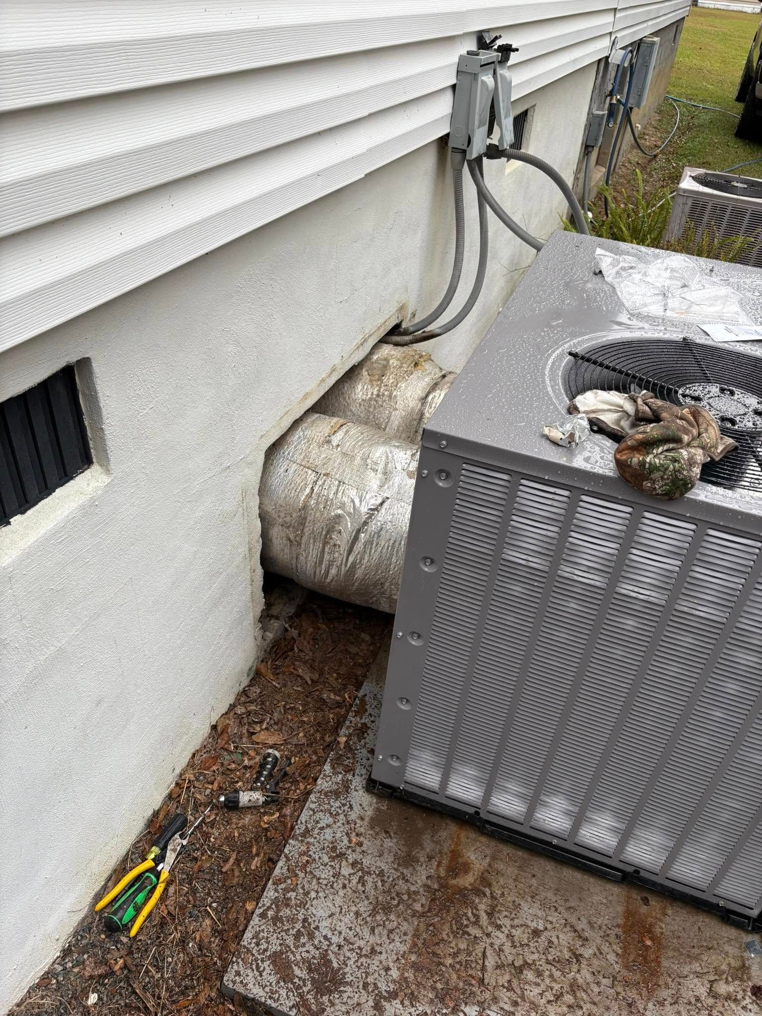 An air conditioner is sitting on the ground next to a house.