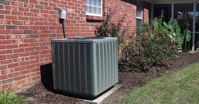 An air conditioner is sitting on the side of a brick house.