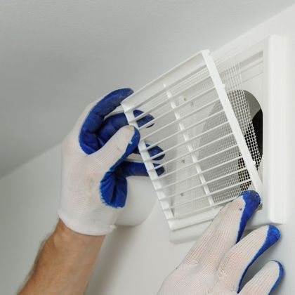 A person wearing blue gloves is working on a vent