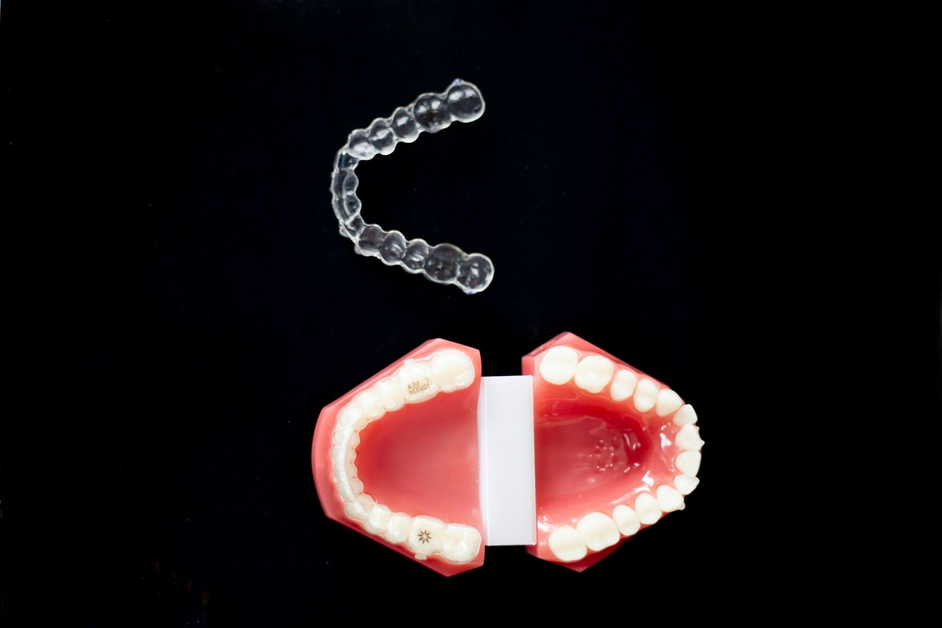 Clear aligner above a model of teeth, both on a black background.