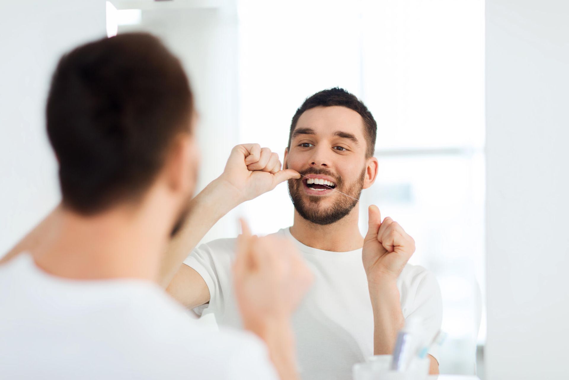 A man is flossing his teeth in front of a mirror.