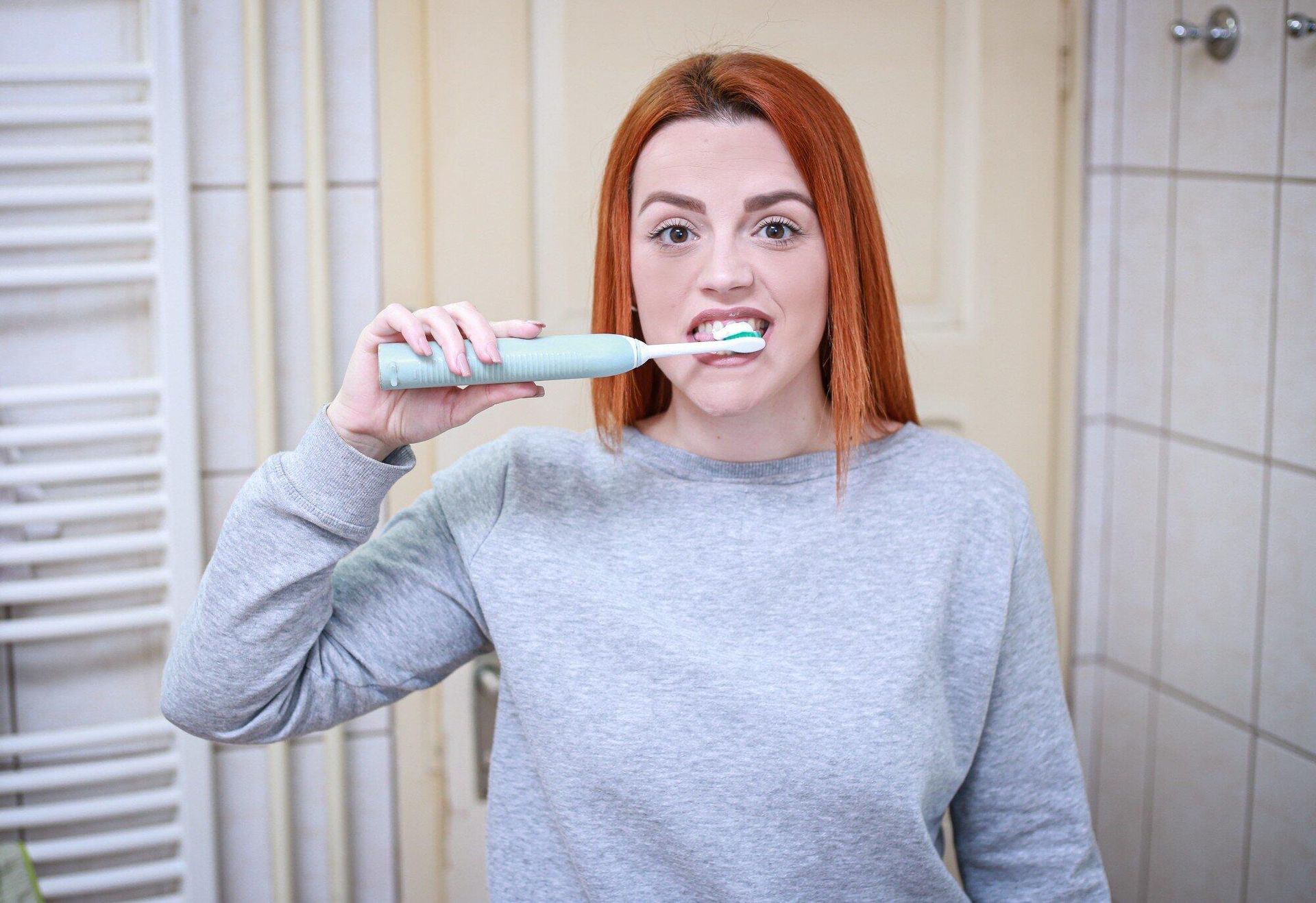 A woman is brushing her teeth with an electric toothbrush in a bathroom.