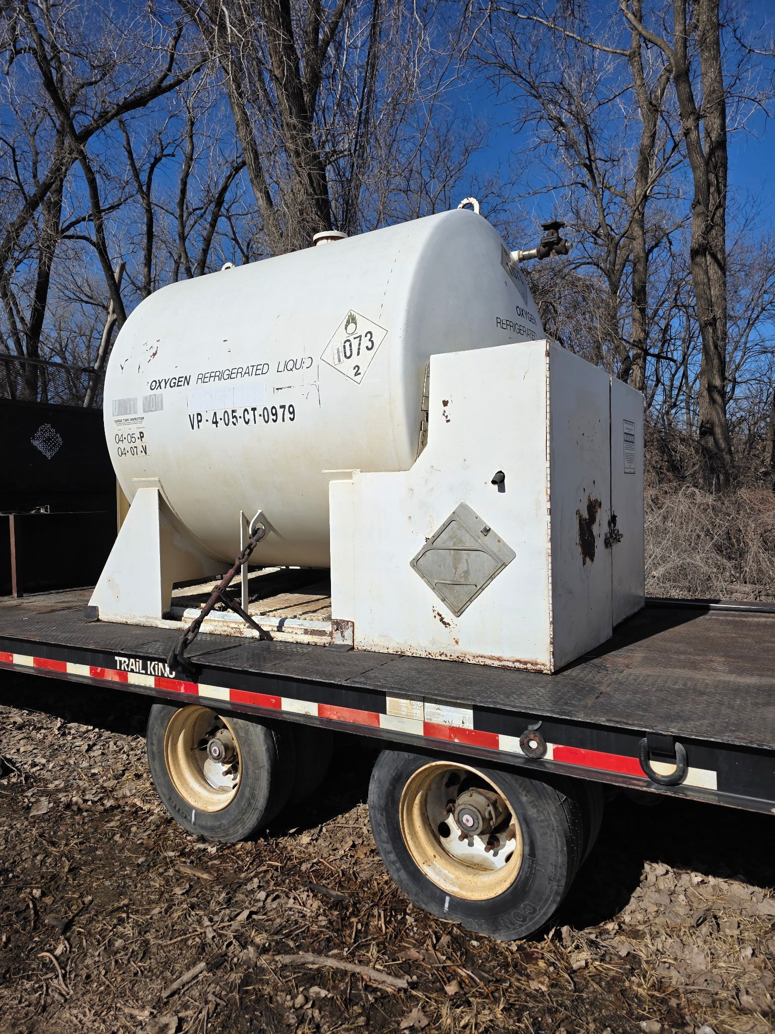 White fuel tank on a trailer with hazardous materials placard.