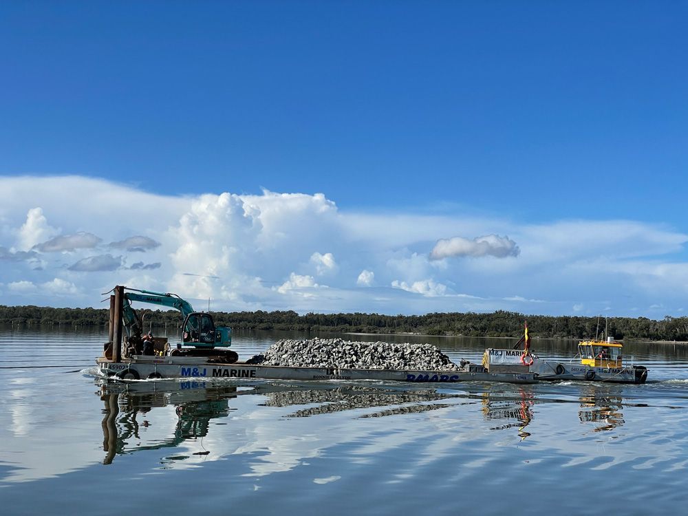 Excavator and Pile of Rocks with Cloudy View — M&J Marine Services in Medowie, NSW