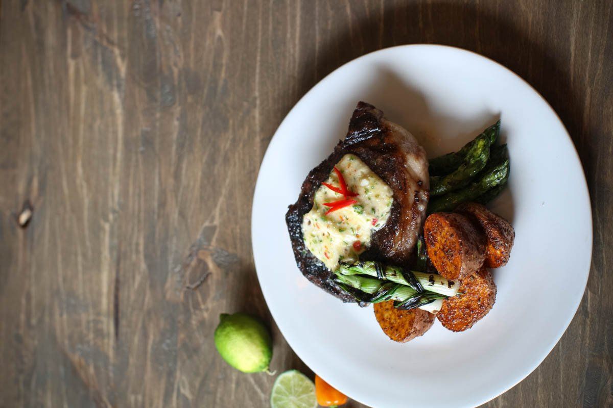 A white plate topped with meat and vegetables on a wooden table.