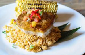 A white plate topped with rice , fish and corn on the cob.