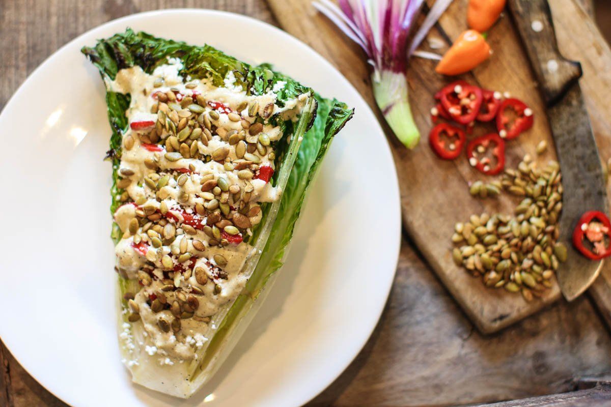 A white plate topped with a slice of lettuce next to a cutting board with vegetables.
