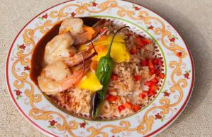 A plate of food with shrimp , rice and peppers on a table.