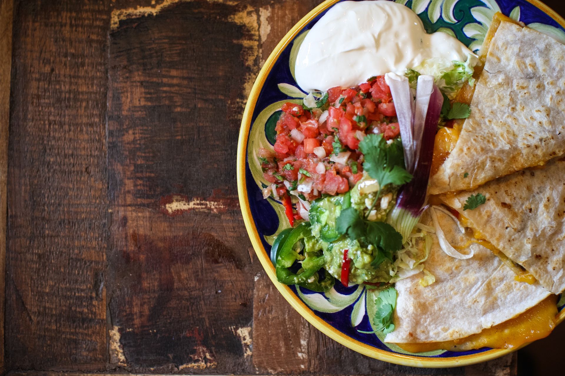 A plate of quesadillas with guacamole and sour cream on a wooden table.