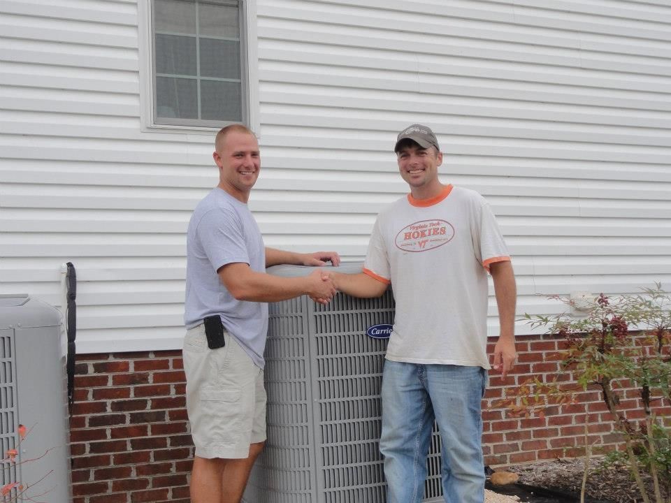 Two men shaking hands in front of an AC unit next to a brick and siding building.best