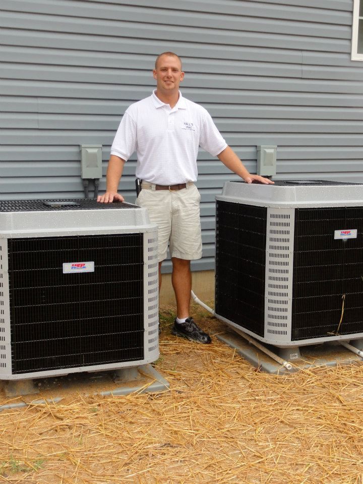 Man standing between two air conditioning units, beige siding in background.