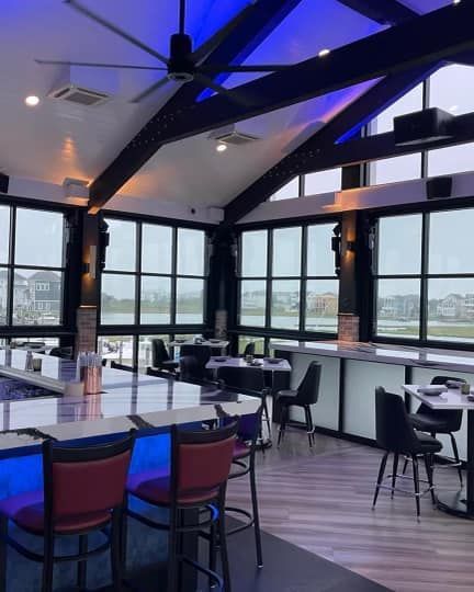 Interior restaurant with bar and seating, large windows, water view. Blue and red lighting.