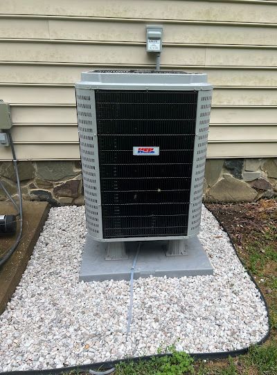 Central air conditioning unit on gravel base, near a beige house wall.