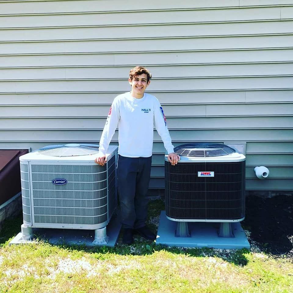 Person stands between two air conditioning units outside a house.