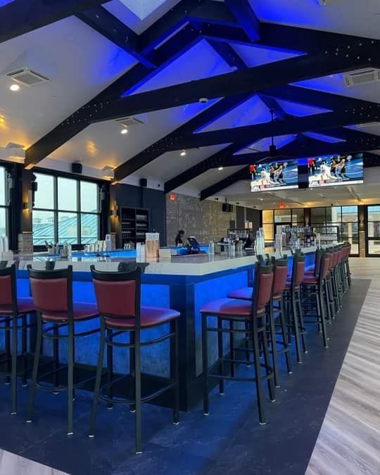 Bar with blue neon lighting, red stools, and a TV; a neutral setting.