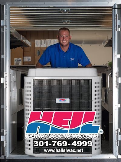 Man in blue shirt smiles behind a large AC unit, inside a truck.