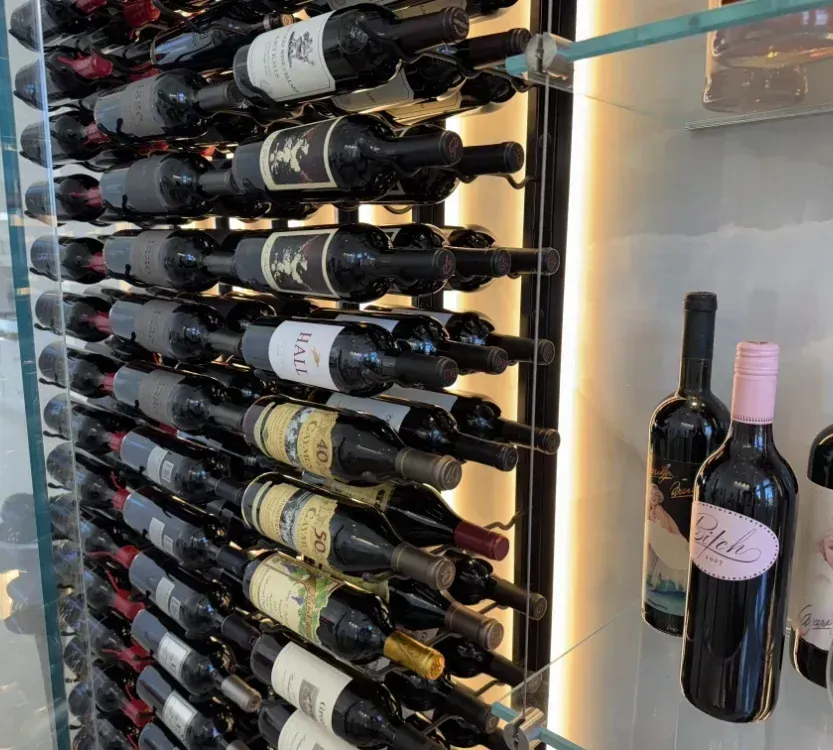 Wine bottles stored in a rack, with glass shelves and ambient lighting.