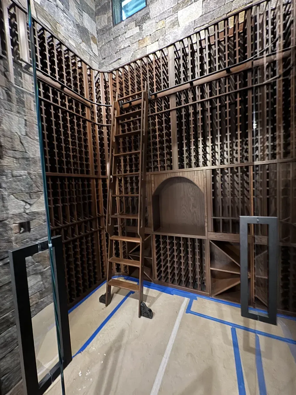 Wine cellar with wooden racks filled with bottles, wooden ladder, and stone wall.
