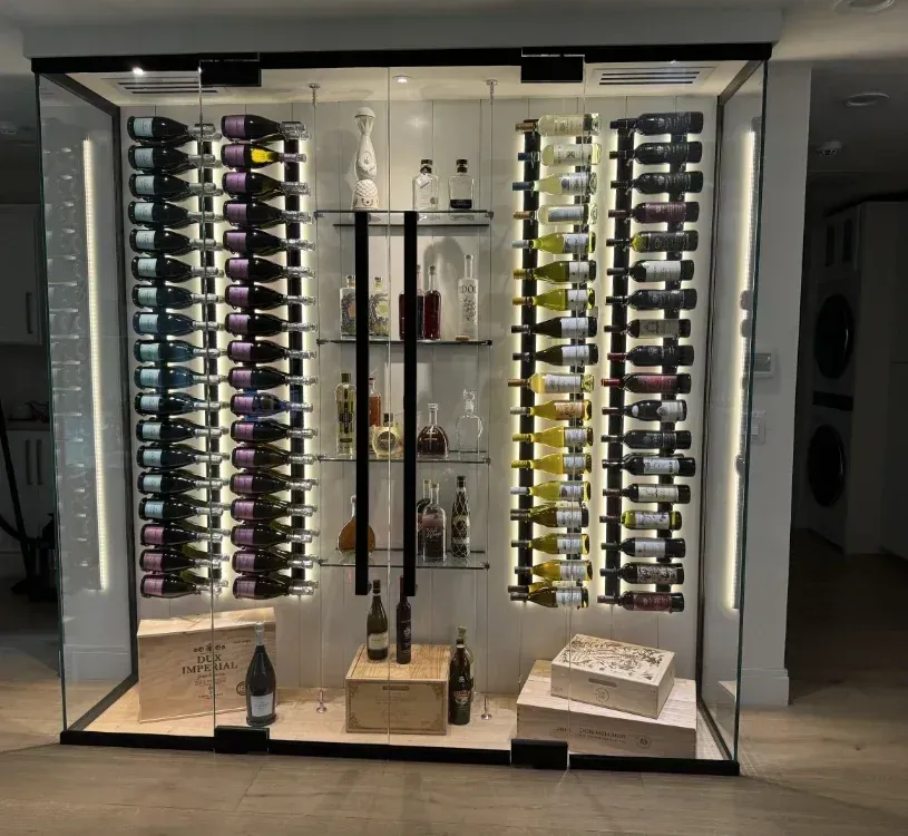 Glass wine cellar with illuminated shelving holding various wine bottles and liquor.