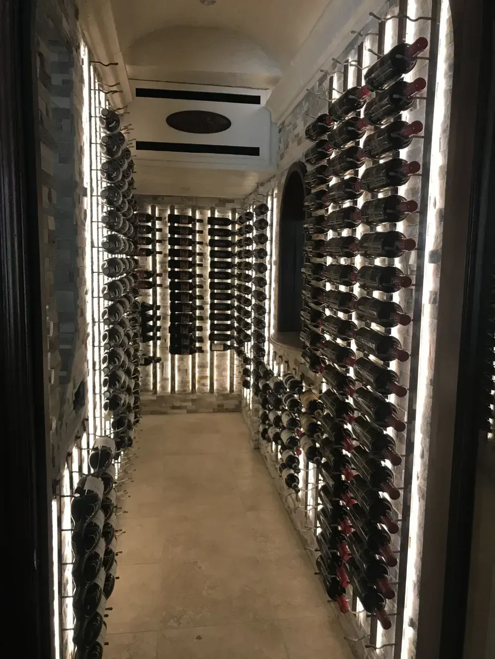 Wine cellar with rows of bottles on metal racks, illuminated by soft white lights.