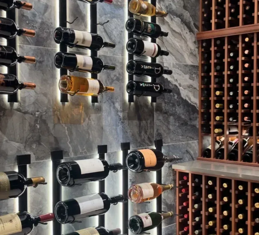 Wine bottles in a modern cellar, mounted on a stone wall. Some bottles are lit by vertical lights; wooden racks on the right.