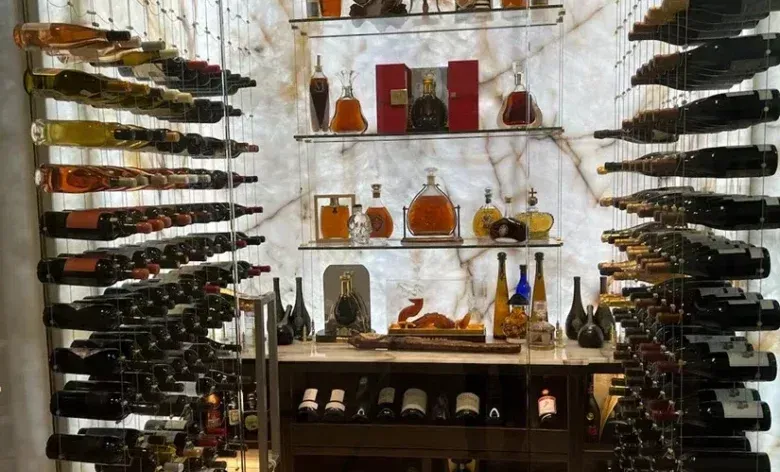 Glass of red wine next to bottle, blurred background of wine bottles and lights.