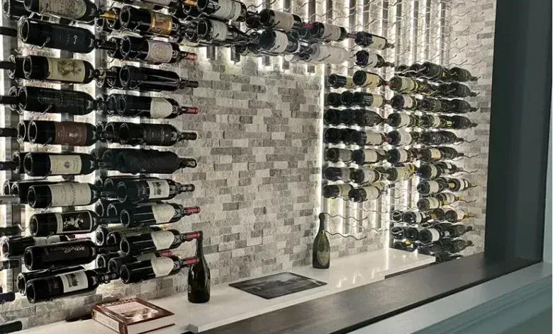 Glass of red wine next to bottle, blurred background of wine bottles and lights.