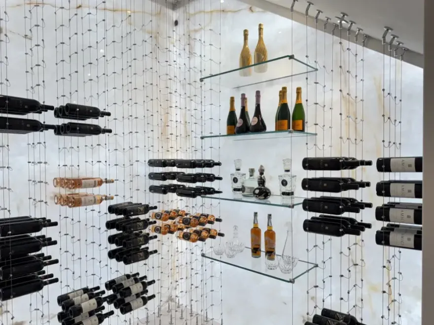 Wine bottles displayed on floating shelves and hanging in front of a textured white wall.