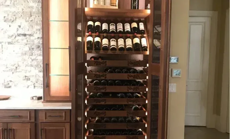 Glass of red wine next to bottle, blurred background of wine bottles and lights.