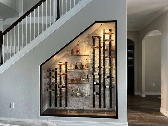 Wine cellar built into the space under stairs, displaying bottles on shelves with lighting.