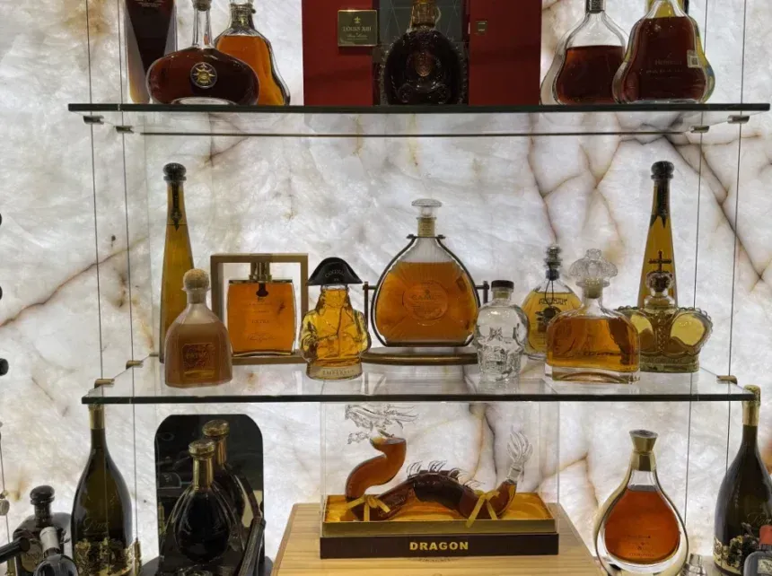 Liquor bottles displayed on glass shelves with marble-like background lighting.