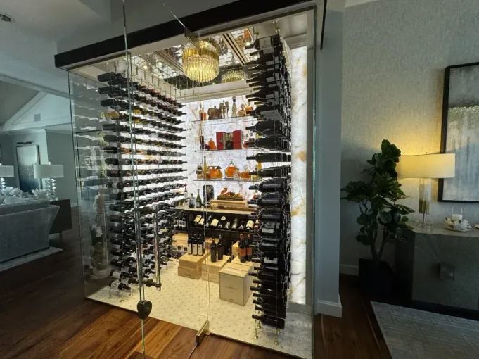 Wine cellar with glass walls, multiple shelves of wine bottles, and decorative lighting.