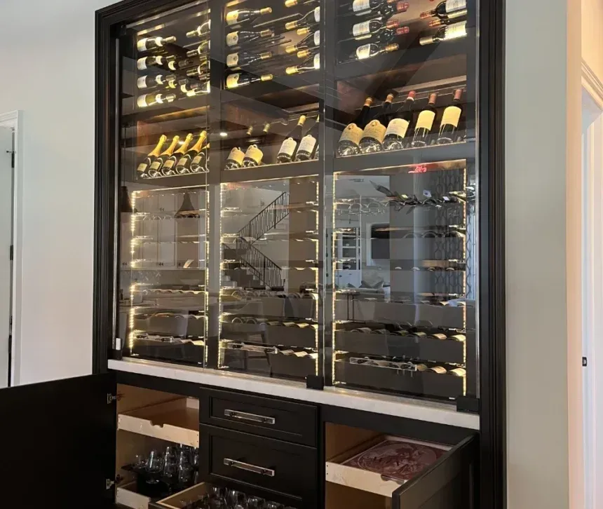 Built-in wine cabinet with glass doors, backlit shelving, and storage drawers; interior lit with wine bottles displayed.