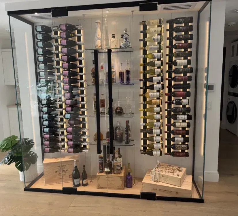 Glass-enclosed wine display with rows of bottles, various liquors on shelves, and wooden crates at the base.