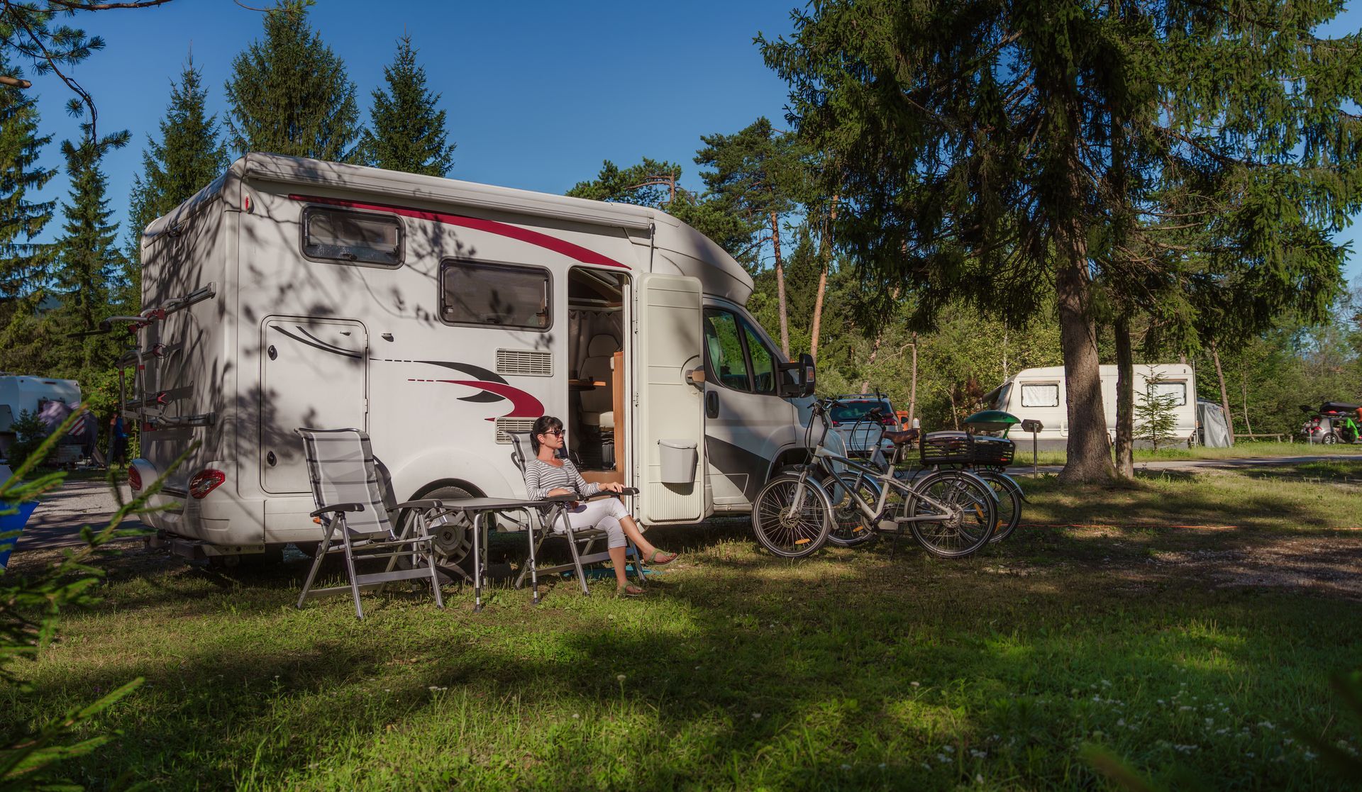 Une femme est assise devant un camping-car garé dans une zone herbeuse.