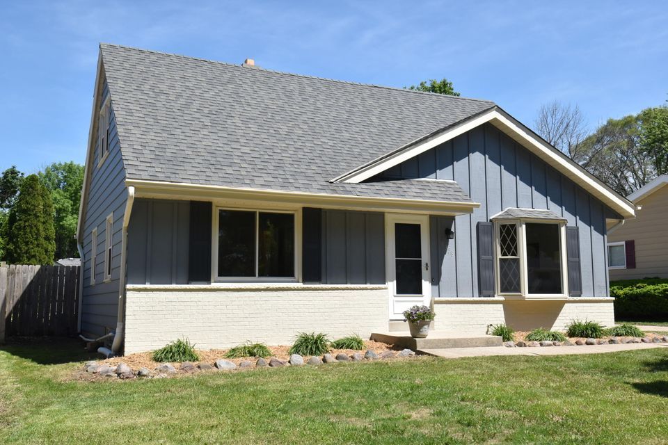A small house with a gray roof and white trim is sitting on top of a lush green lawn.