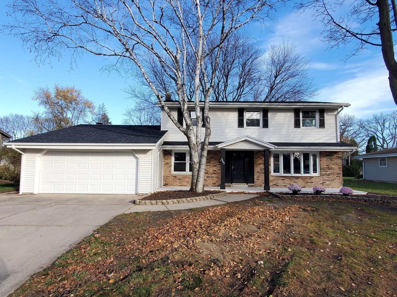 A large brick house with a white garage door and a tree in front of it.