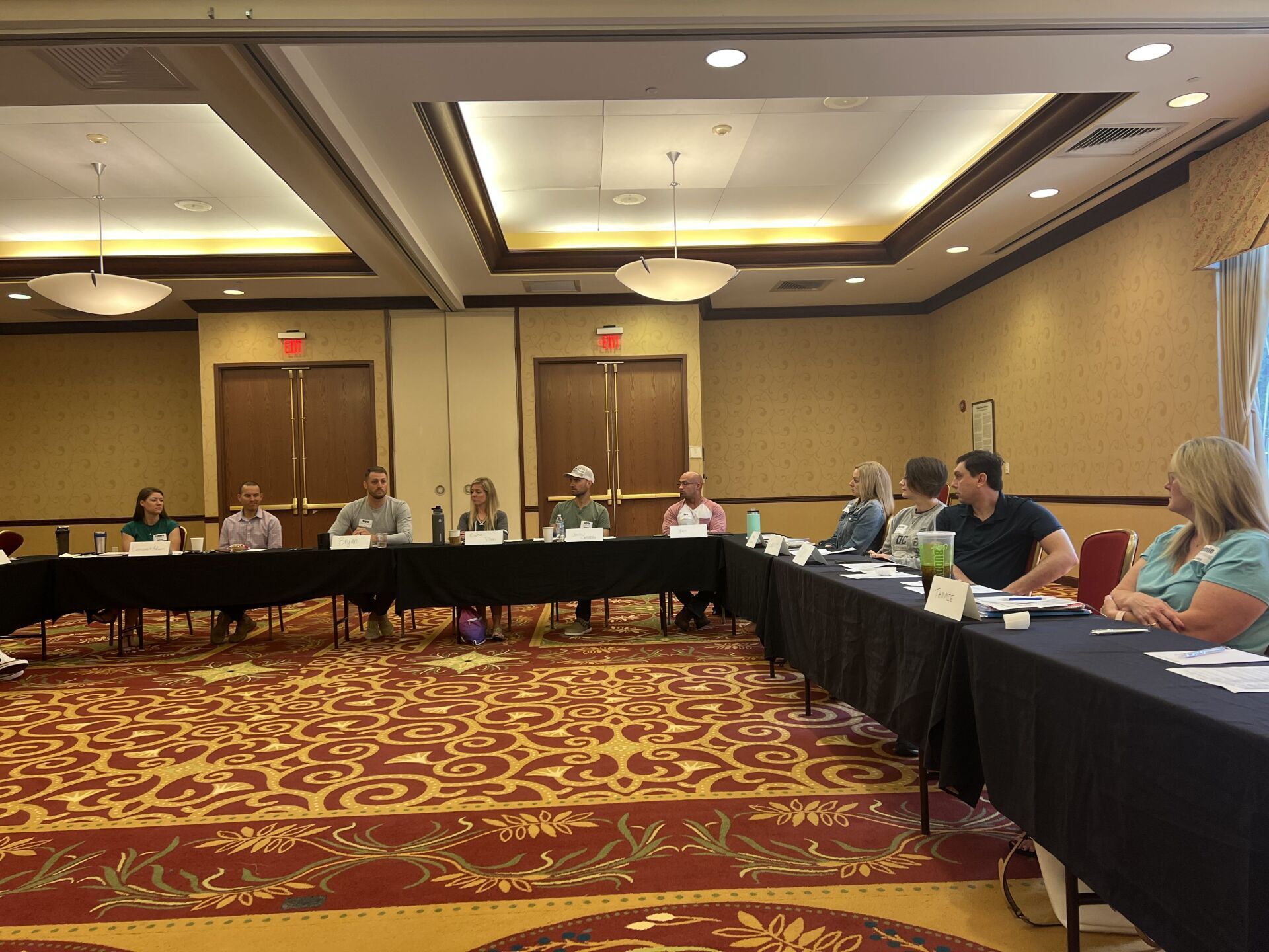A group of people are sitting at long tables in a conference room.