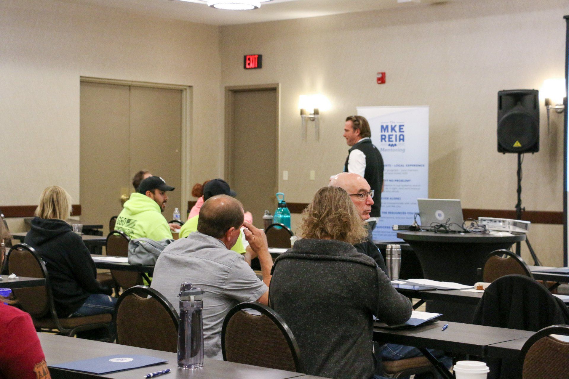 A group of people are sitting at tables in a room with a sign that says meet rea